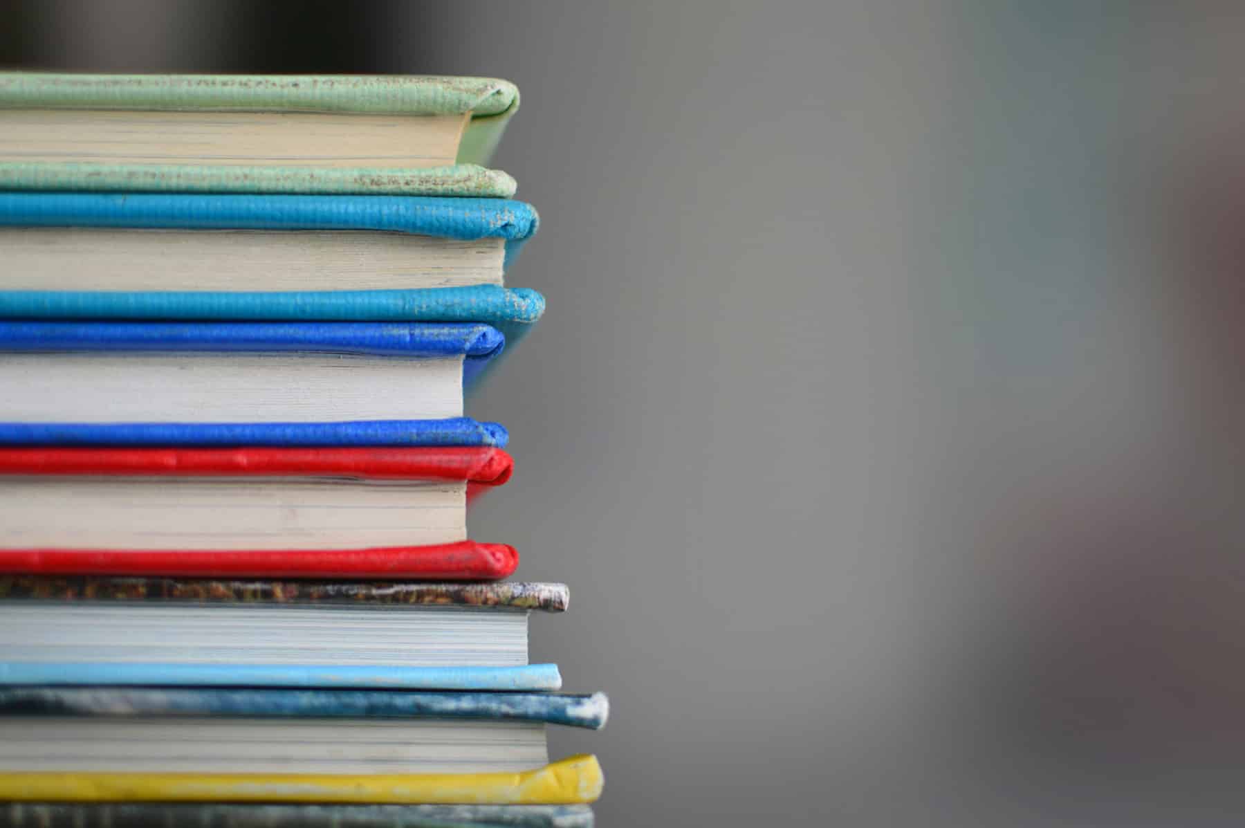 Pile of books each with different colour covers in focus with blurred background